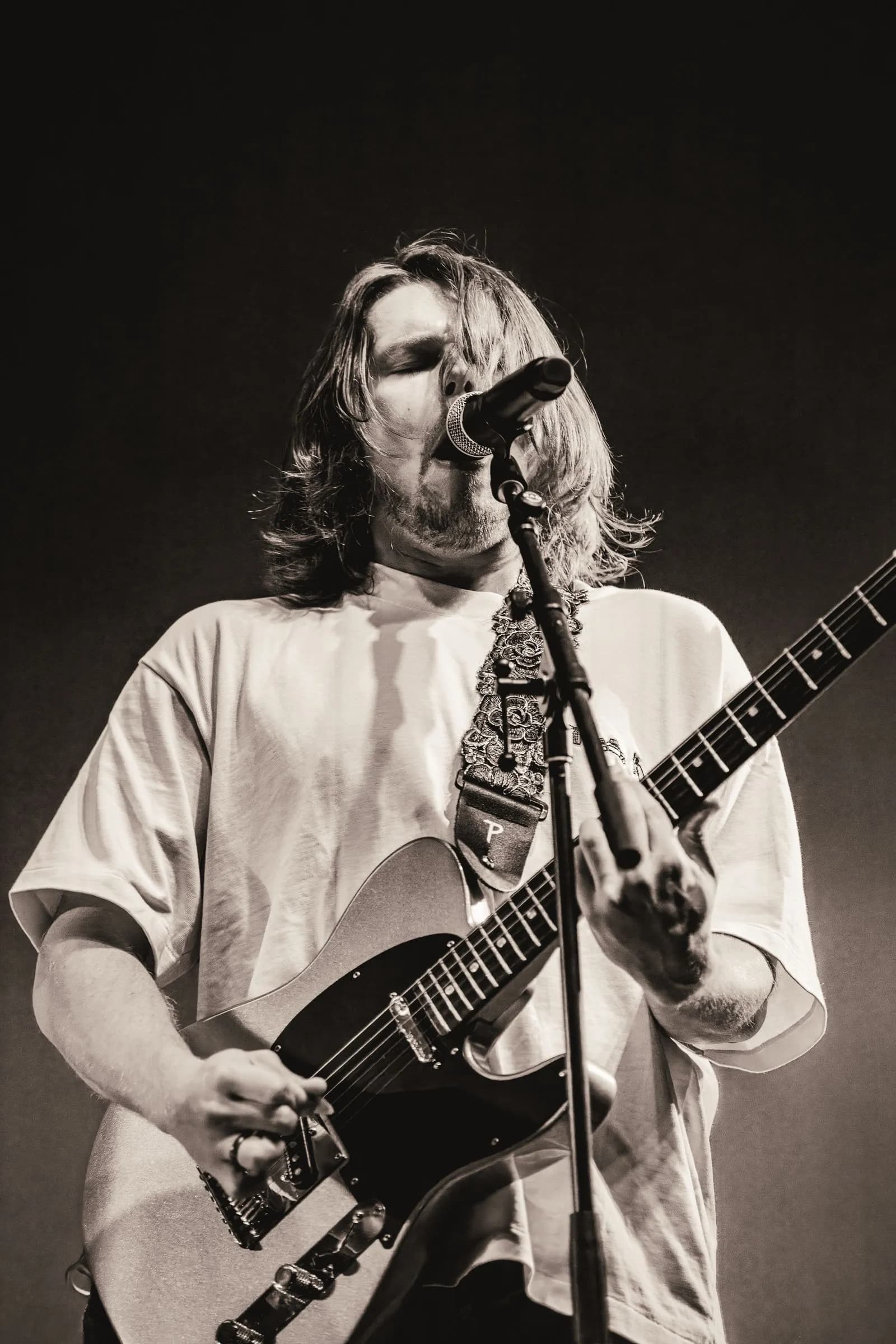 Black-and-white photo of Cigarettes @ Sunset's singer belting into the mic while playing guitar