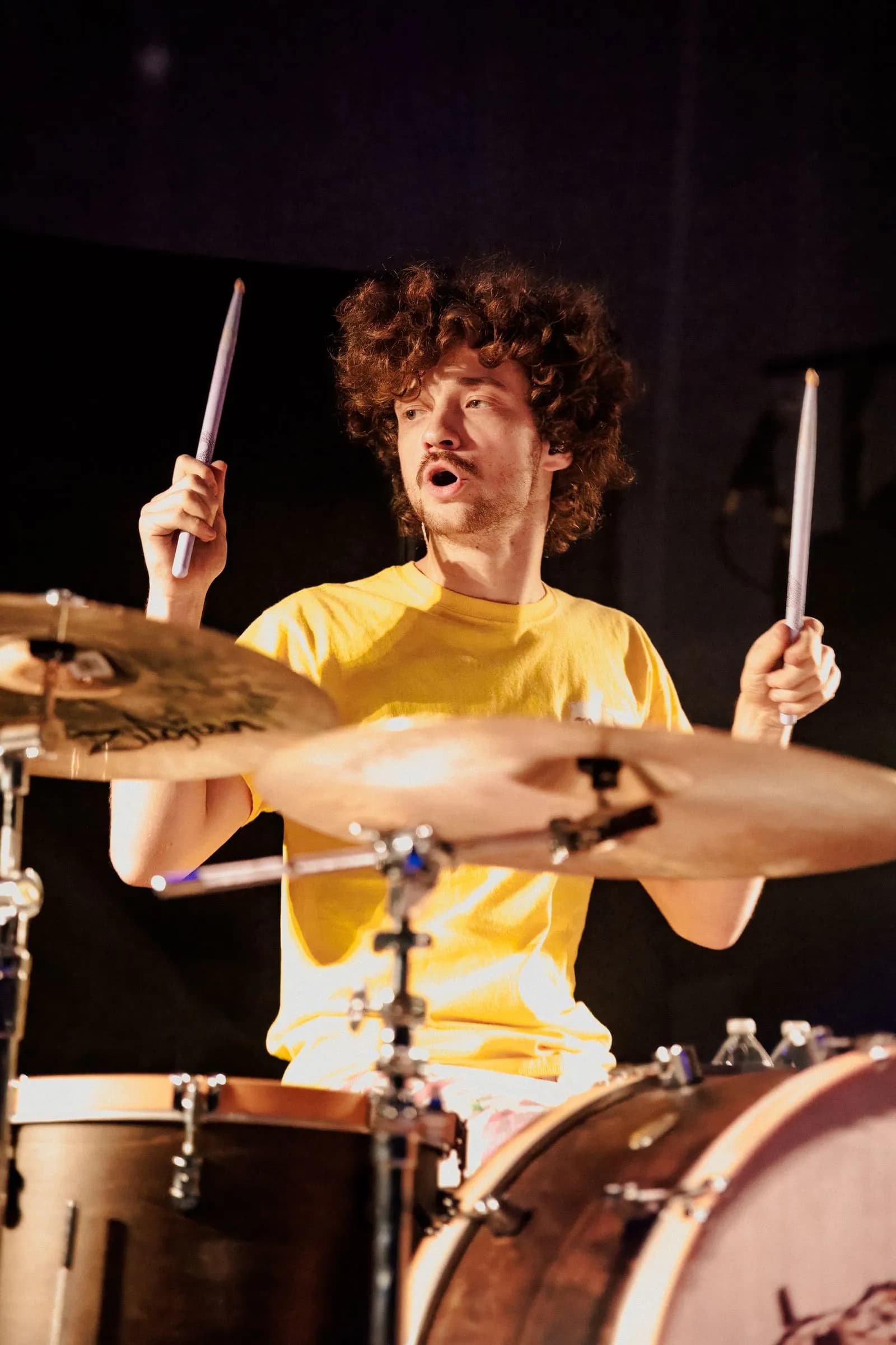 Cigarettes @ Sunset's curly-haired drummer in a yellow shirt raises both sticks behind the cymbals