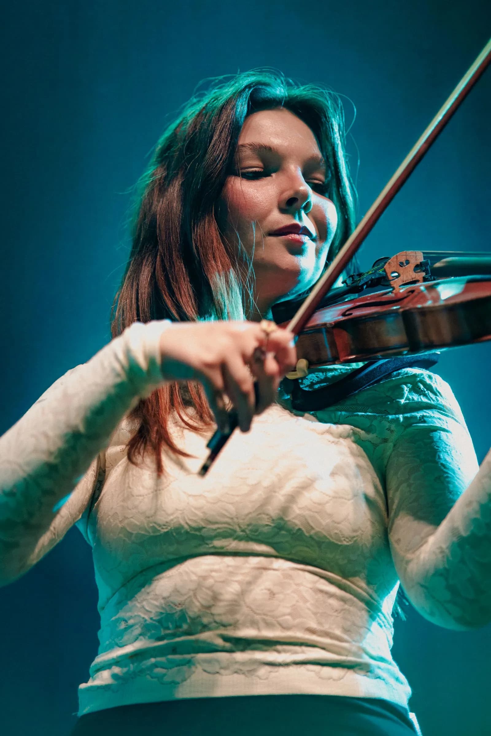 Cigarettes @ Sunset's fiddle player draws the bow under teal stage light