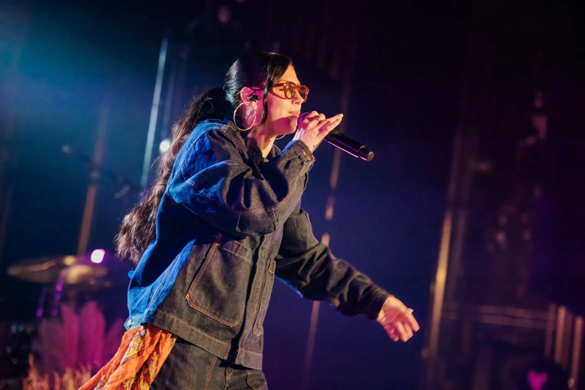 Lizzie Morgan leans into a song, microphone in hand, under deep blue and purple stage light