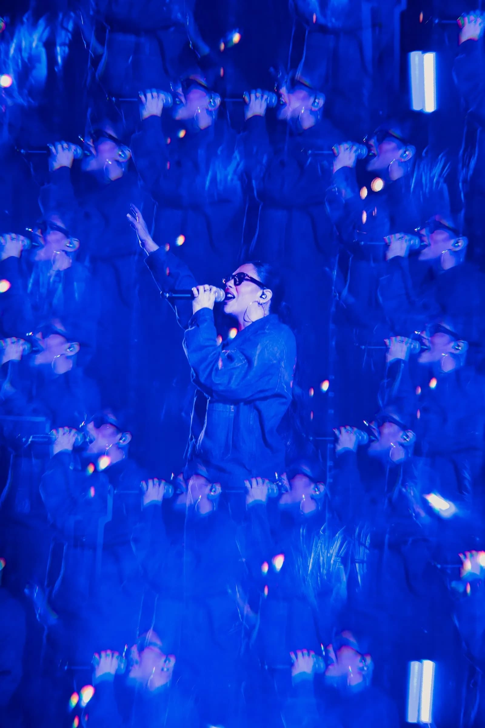 Multiple-exposure image of Lizzie Morgan singing, repeated across a field of blue light