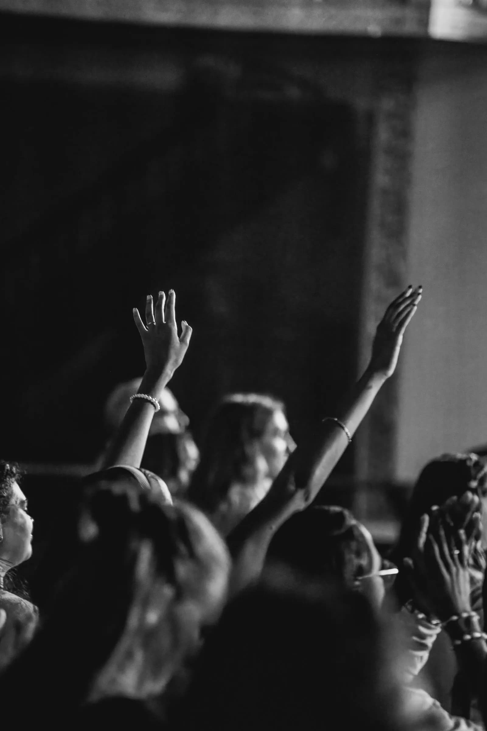 Black-and-white photo of audience members raising their hands in worship