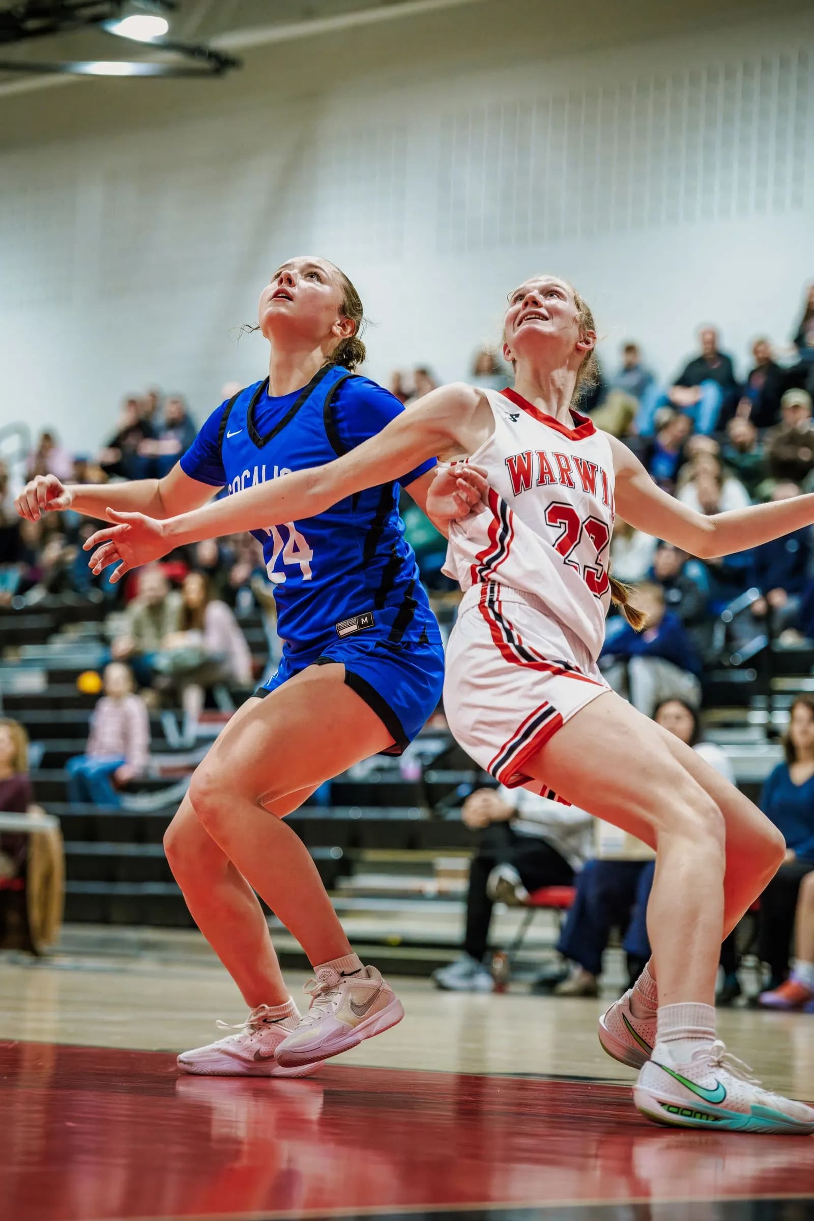 Two female basketball players defend on an illuminated indoor court, eyes lifted toward the ceiling.