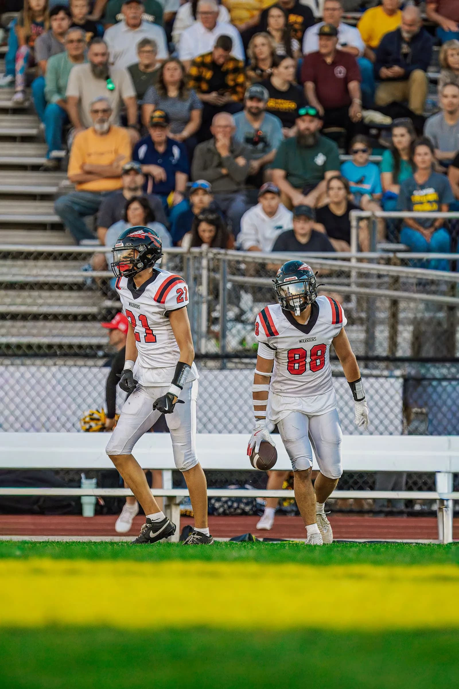 American football players run on an outdoor field as a player in a white jersey with number 88 holds a football.
