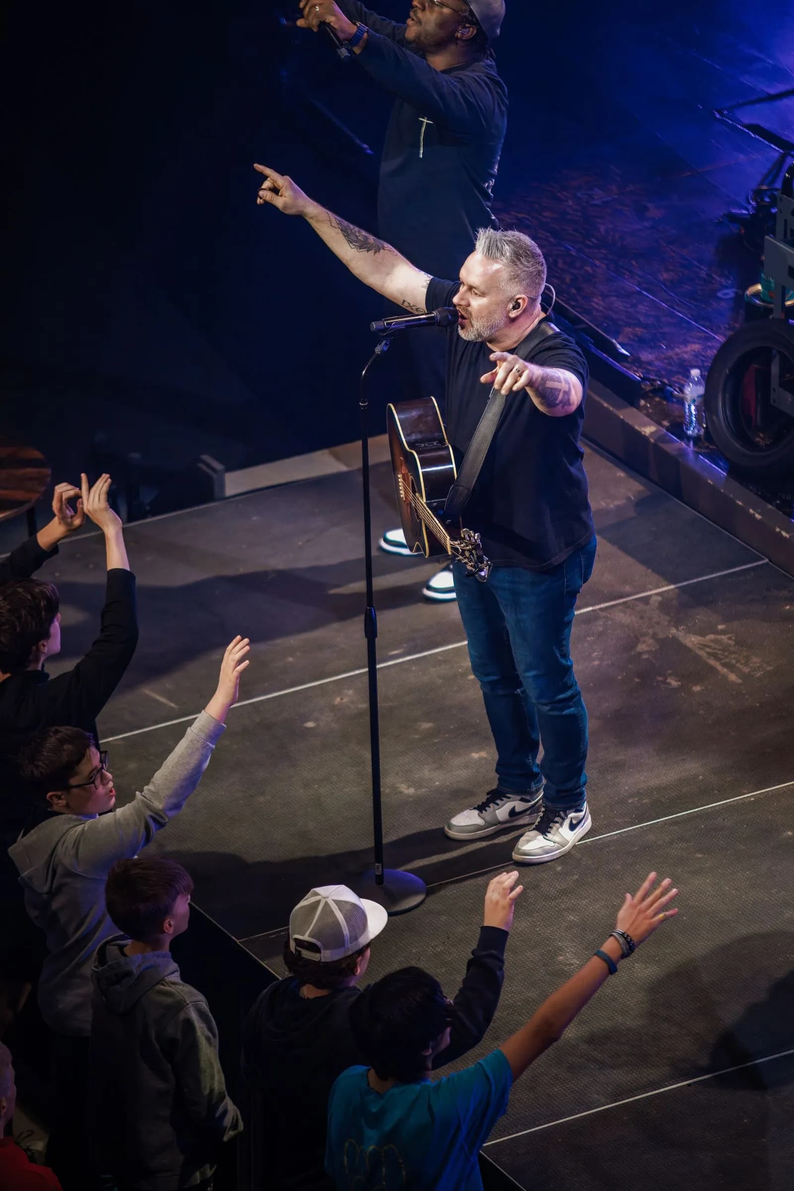 A man sings into a microphone and points at the audience on stage at LCBC Manheim.