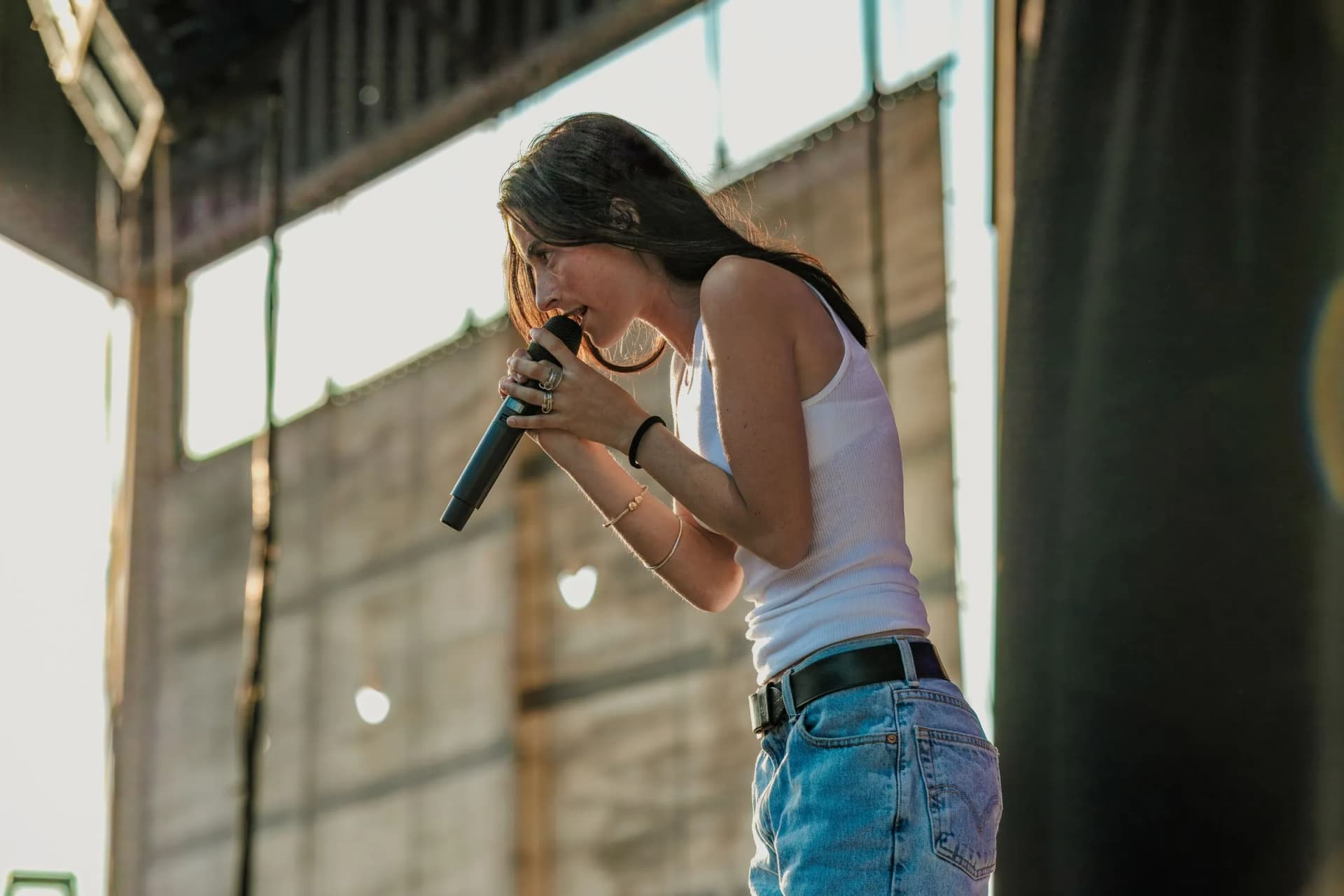 Stella Lefty sings on an outdoor stage with a black microphone, rings and bracelets visible.